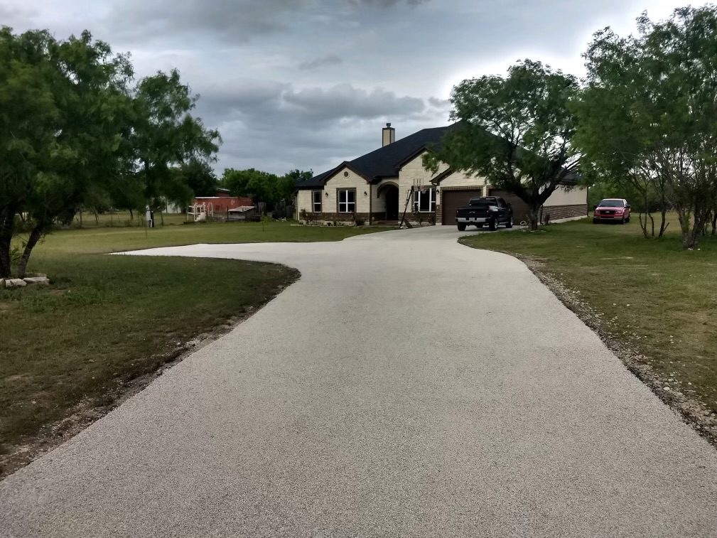Light-colored chip seal driveway curving toward a home and garage.